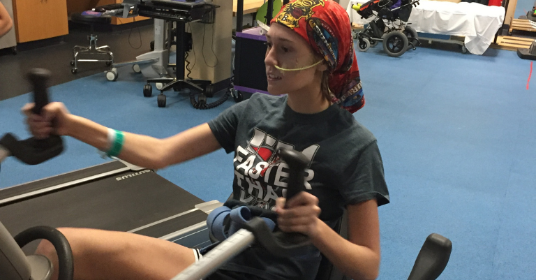traumatic brain injury patient in red, gold, and green bandana exercising on a recumbent bike