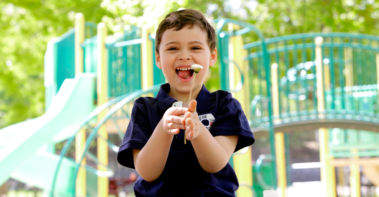 Young boy at a playground, smiling and playing with a dandelion